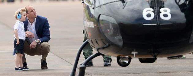 Prinz William hockt mit seinem Sohn Prinz George vor einem Hubschrauber Prinz William hockt mit seinem Sohn Prinz George vor einem Hubschrauber